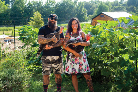 a man and a woman each holding a turkey standing in a garden
